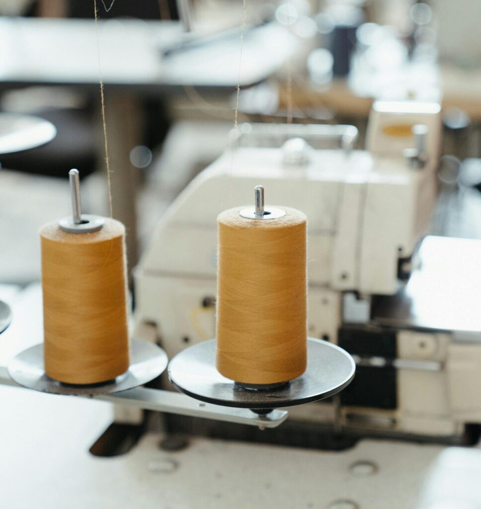Detailed view of a sewing machine with spools of thread in a workshop setting.